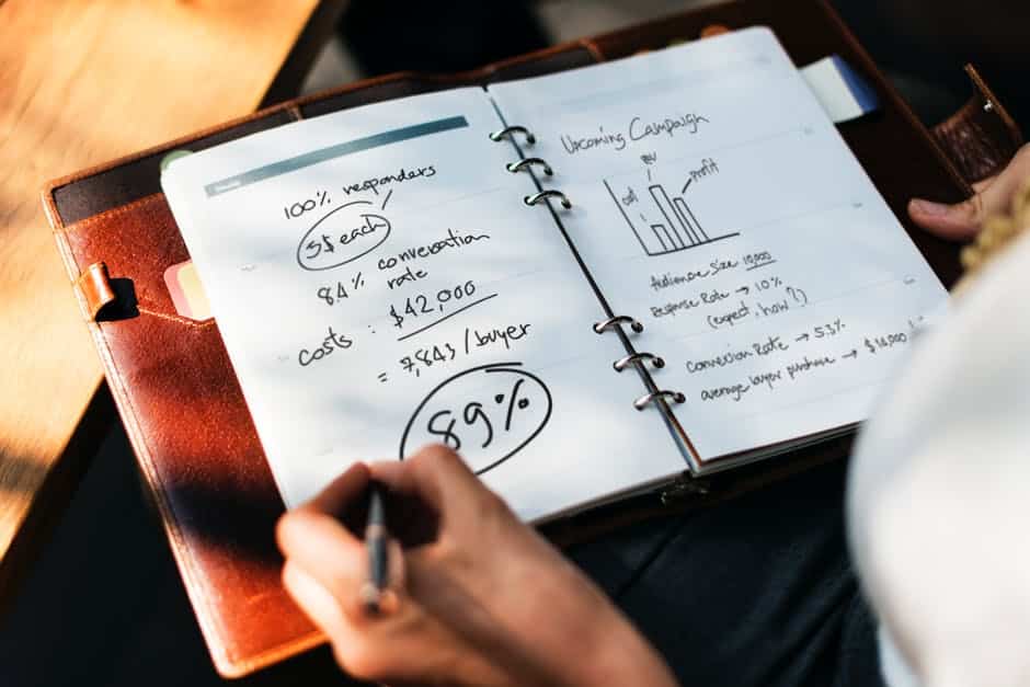 Person Holding Pen in Front of Open Book Planner