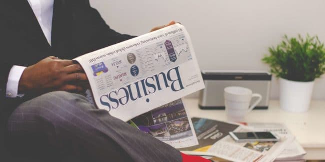 man-reading-newspaper-while-sitting-near-table-with-935979